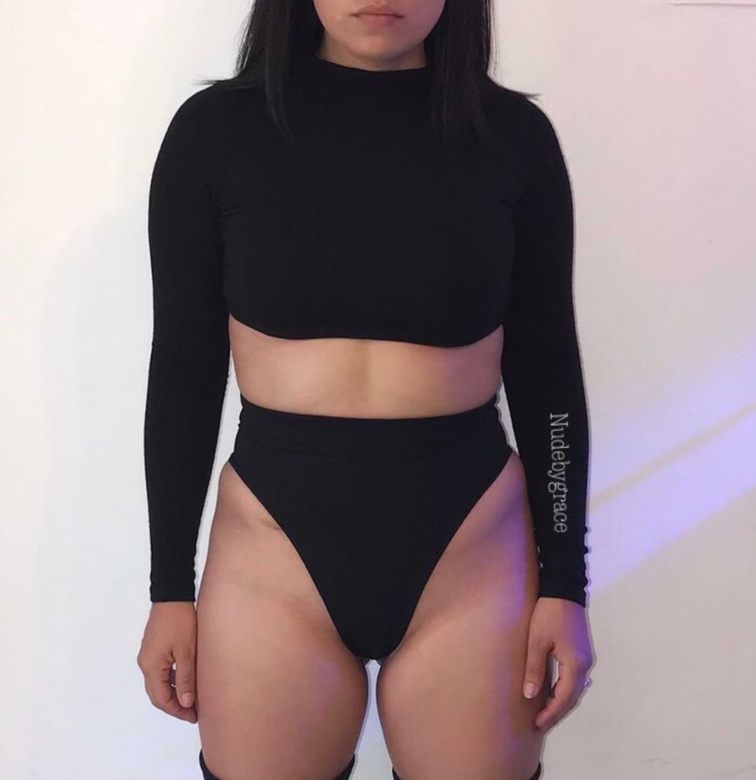 Woman modeling a long sleeve two-piece swimsuit in solid black with a high-waisted bottom and fitted crop top.